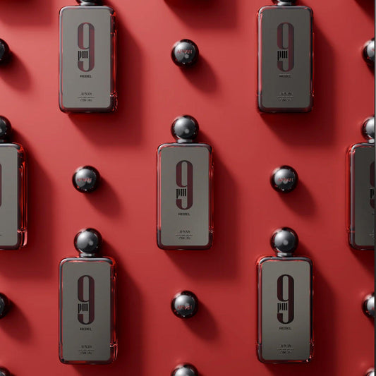 Afnan 9PM Rebel perfume bottles arranged in a neat pattern on a bold red background, featuring sleek black design with spherical caps, reflecting modern and confident style