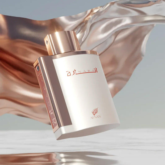 Afnan Naram Eau De Parfum bottle in elegant white and rose gold design displayed against a flowing metallic fabric background with soft lighting