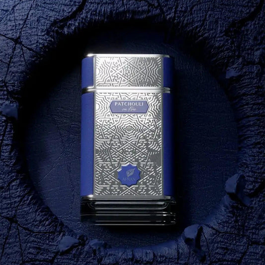 Afnan Patchouli On Fire Eau De Parfum bottle with intricate silver and blue design displayed on a textured dark blue surface with artistic lighting
