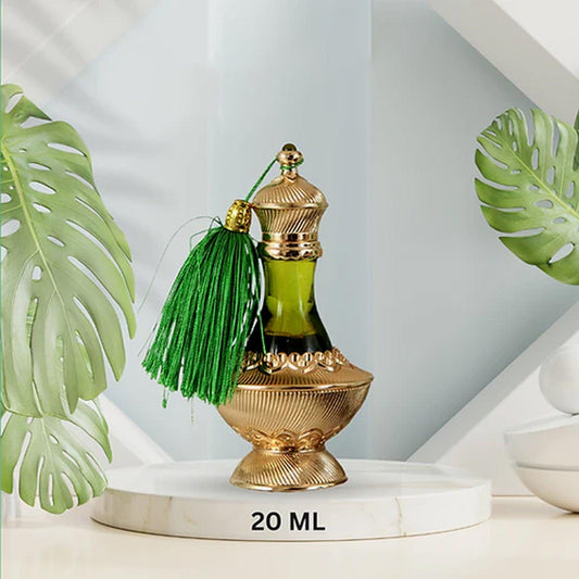 Luxury 20ml attar bottle with gold detailing and green tassel displayed on a marble platform surrounded by tropical leaves in a modern setting