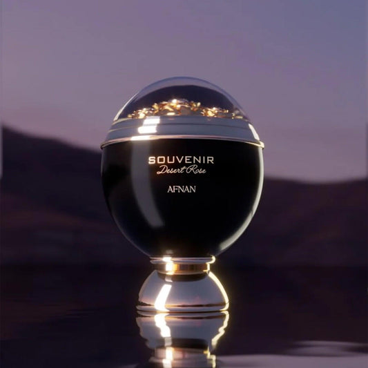 Afnan Souvenir Desert Rose Eau De Parfum spherical black and gold bottle displayed on a reflective surface with a sunset desert background