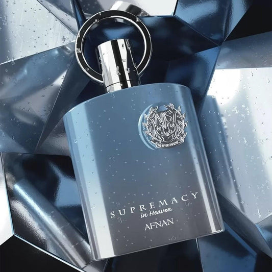 Afnan Supremacy in Heaven perfume bottle in sleek metallic blue with a silver emblem, placed against a reflective ice-blue textured background evoking freshness and luxury