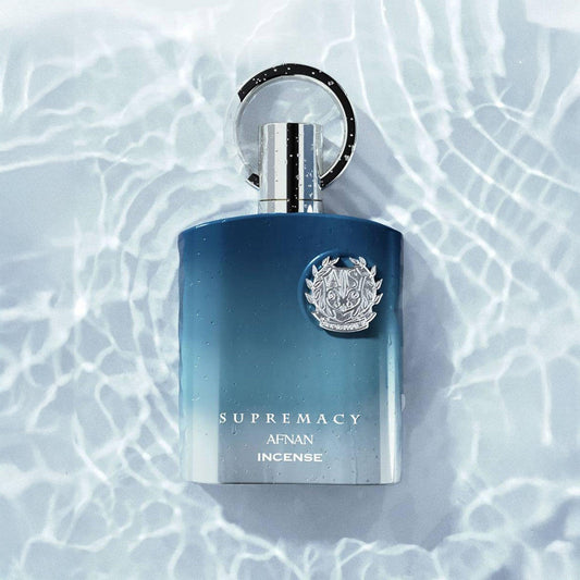 Afnan Supremacy Incense Eau De Parfum bottle in gradient blue and silver design displayed on a rippling water surface with sunlight reflections
