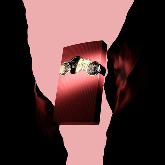 Afnan Tribute Pink Eau De Parfum bottle in deep red with gold detailing illuminated dramatically against a pink and black abstract background