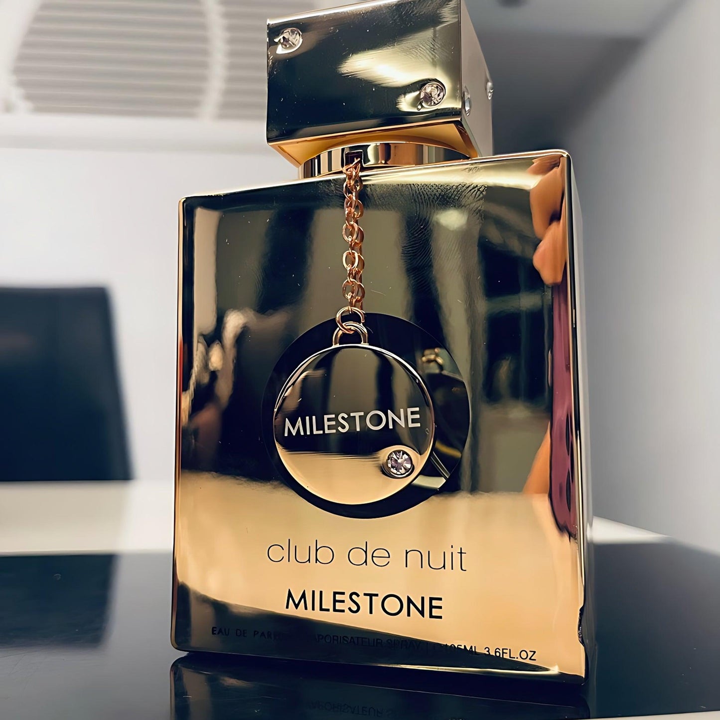 Armaf Club De Nuit Milestone Eau De Parfum gold reflective bottle with metallic chain emblem displayed on a modern tabletop background