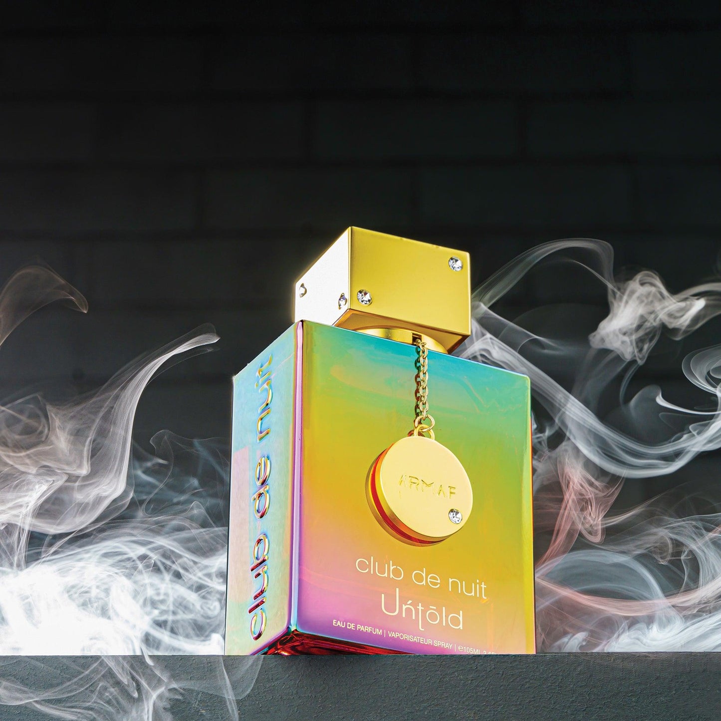 Armaf Club De Nuit Untold Eau De Parfum bottle with gold cap and iridescent body surrounded by smoke against a dark background