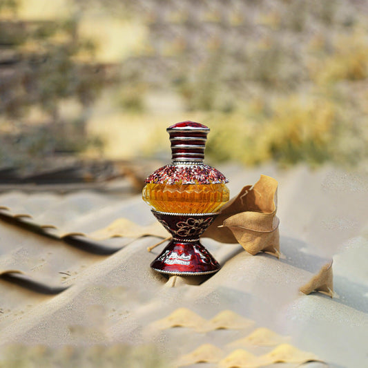 Asgharali perfume in ornate red and gold bottle placed on textured beige surface with dried leaves in the background