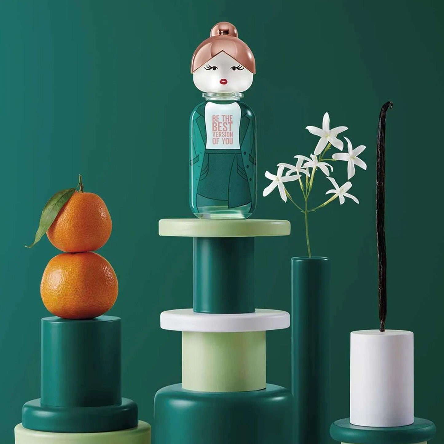 United Colors of Benetton Be The Best Version of You perfume bottle designed as a green doll displayed on geometric pedestals with tangerines, jasmine flowers, and a vanilla pod