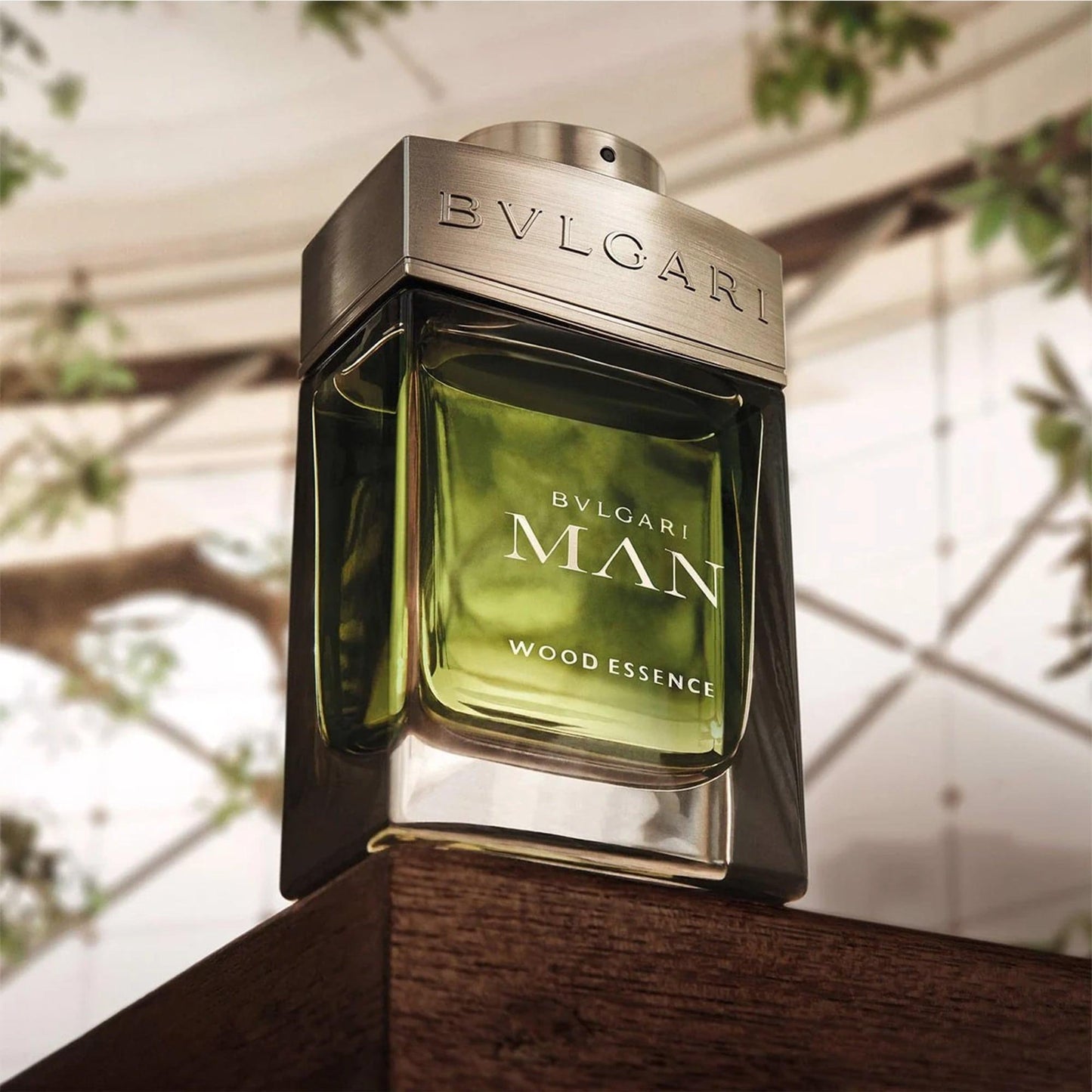Bvlgari Man Wood Essence Eau De Parfum green glass bottle with metallic cap placed on wooden surface and blurred nature background