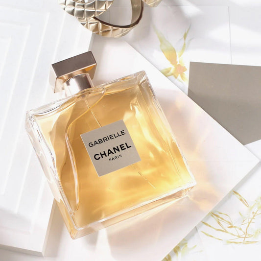 Chanel Gabrielle perfume bottle on white background with golden glow and sunlight reflections.