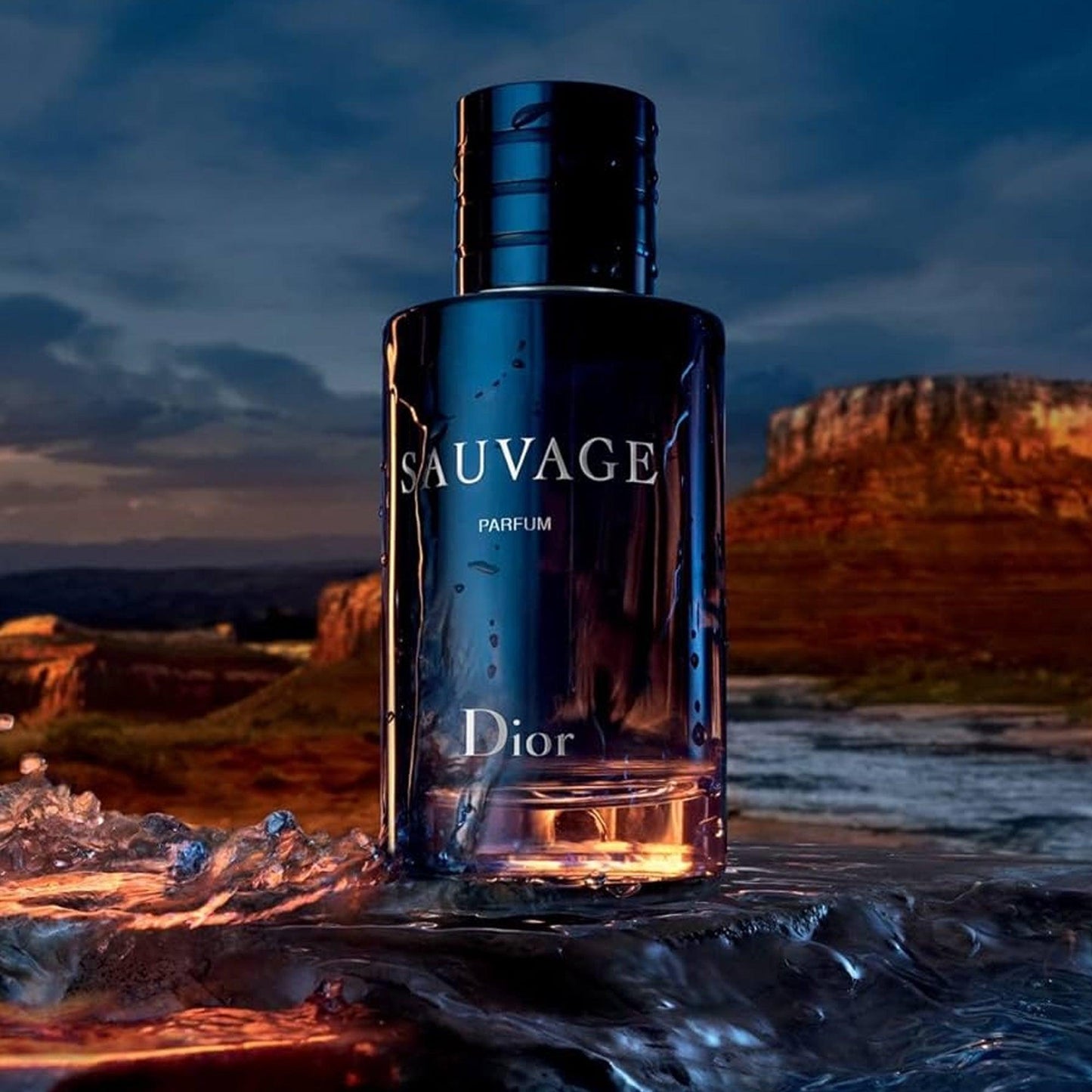 Dior Sauvage Parfum dark blue bottle placed on wet rocky surface with water reflections and scenic desert landscape in the background at sunset