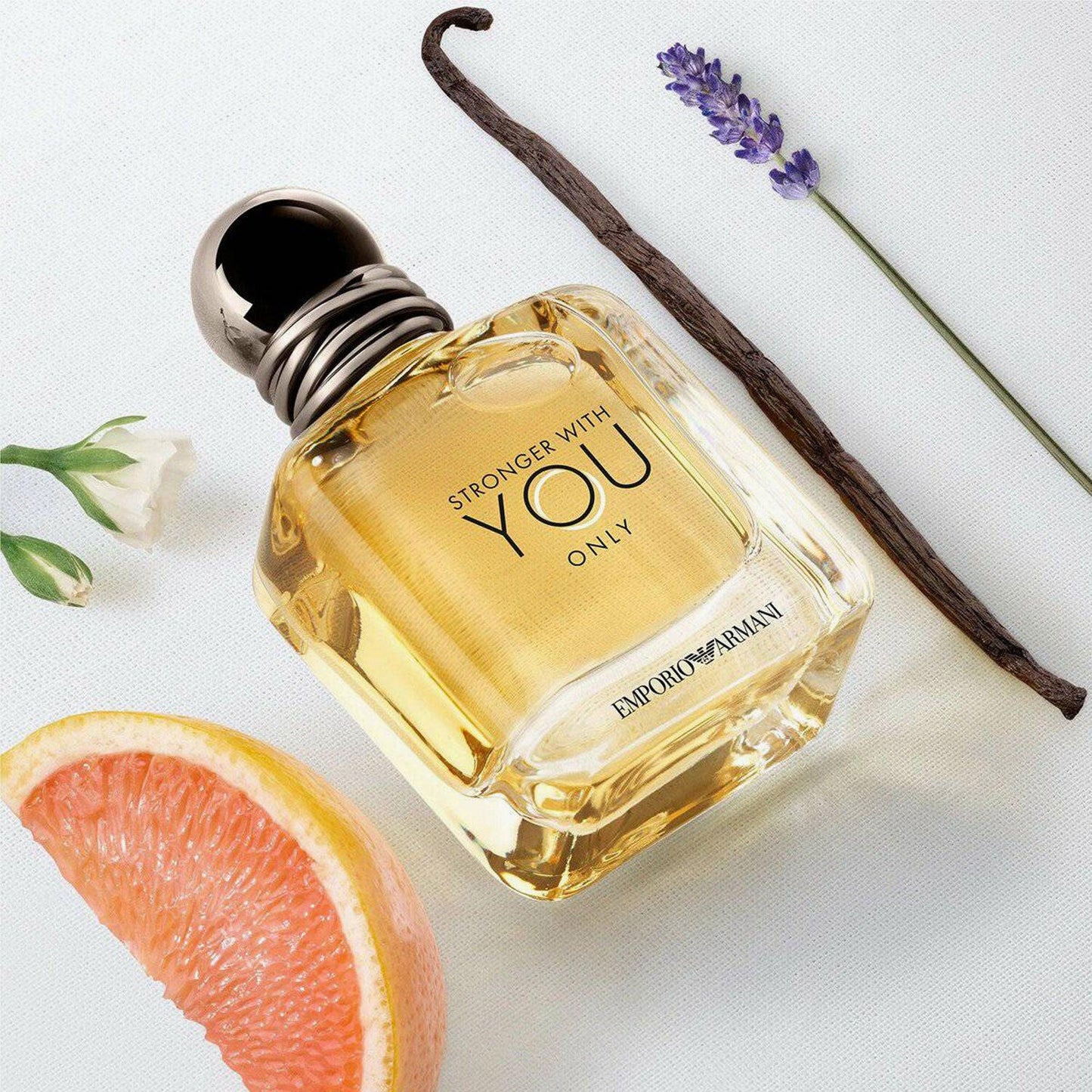 Emporio Armani Stronger With You Only Eau De Toilette bottle placed on a white surface with grapefruit slice, lavender, vanilla pod, and white flower.