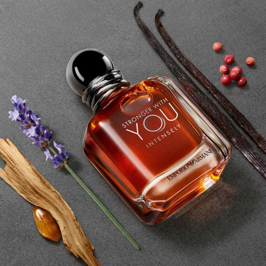 Emporio Armani Stronger With You Intensely Eau De Parfum bottle placed on a grey surface surrounded by vanilla pods, lavender, wood, amber, and peppercorns