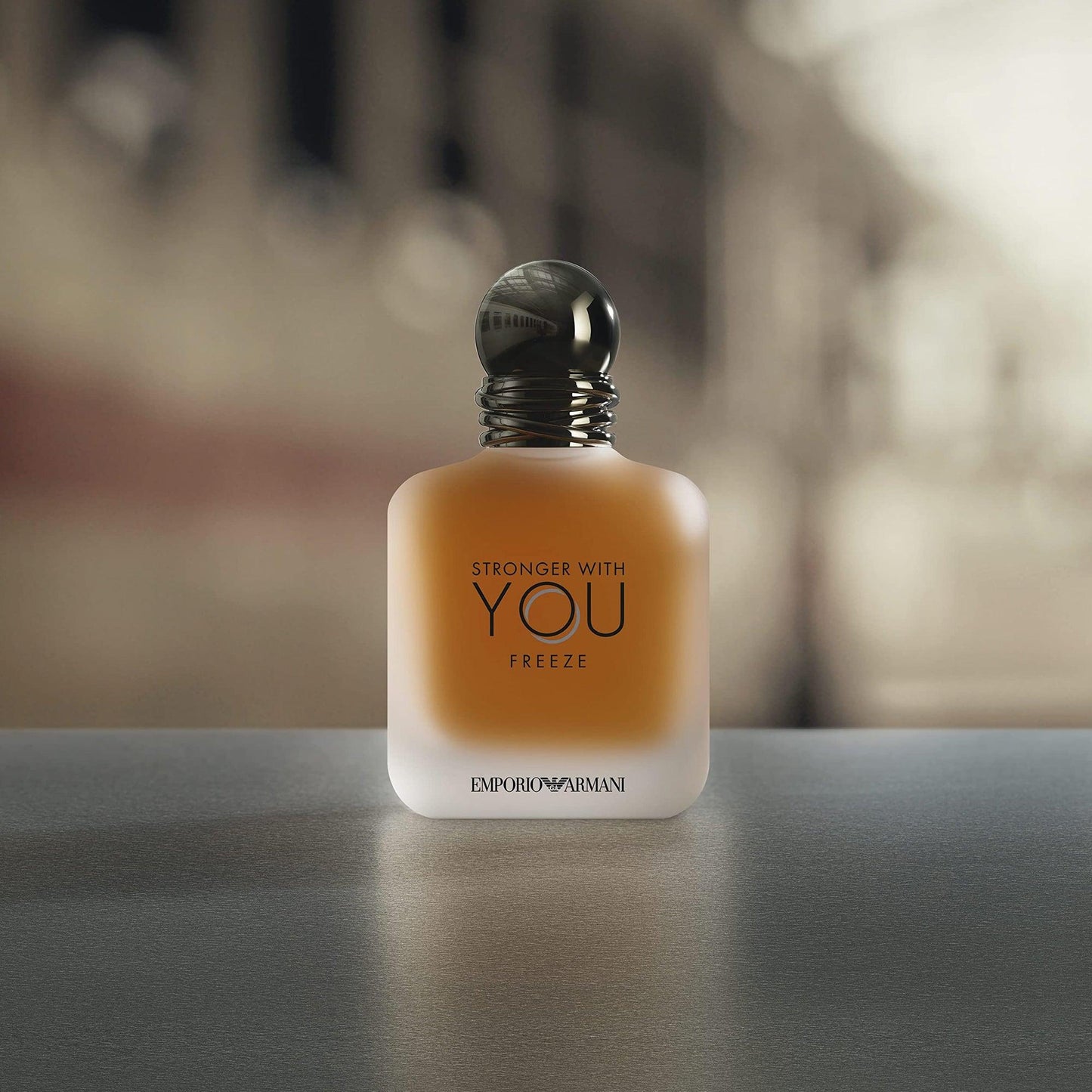 Emporio Armani Stronger With You Freeze Eau De Toilette frosted glass bottle with amber liquid placed on a smooth gray surface and blurred background
