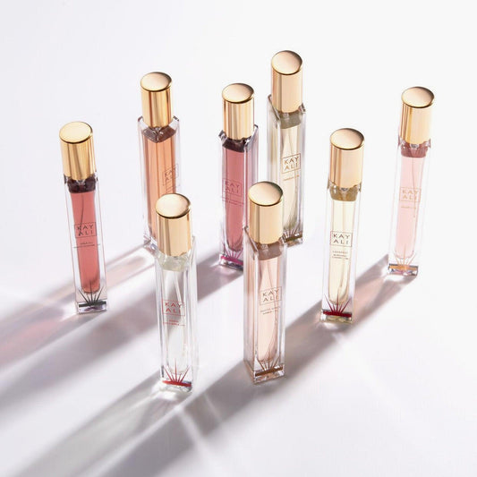 Kayali perfume travel-size collection featuring multiple fragrances in slim glass bottles with gold caps arranged on a bright white background.
