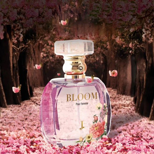 J. Bloom Pour Femme perfume bottle placed in a dreamy floral pathway with pink petals and blooming flowers around.