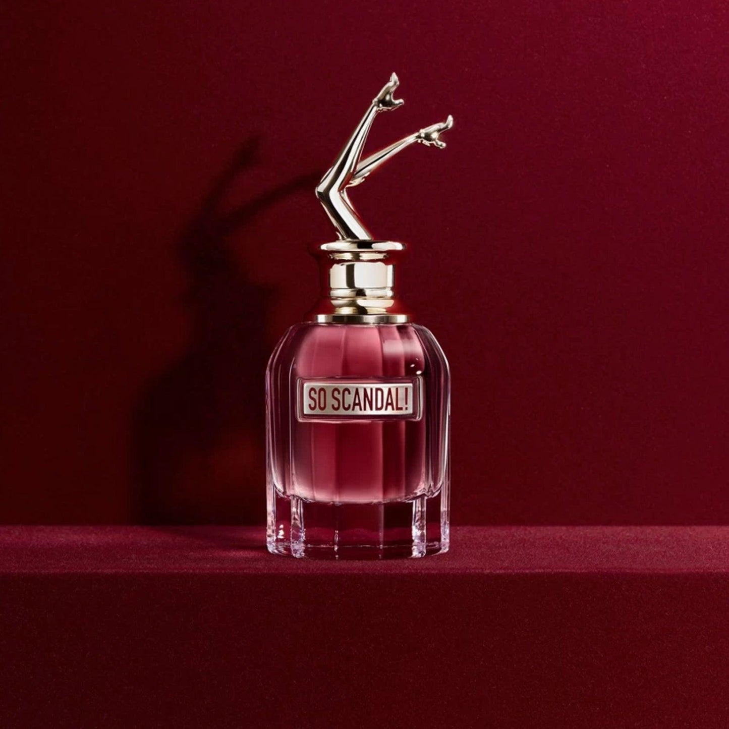 Jean Paul Gaultier So Scandal! Eau De Parfum with a playful leg-shaped cap, placed on a red velvet surface with a deep red background