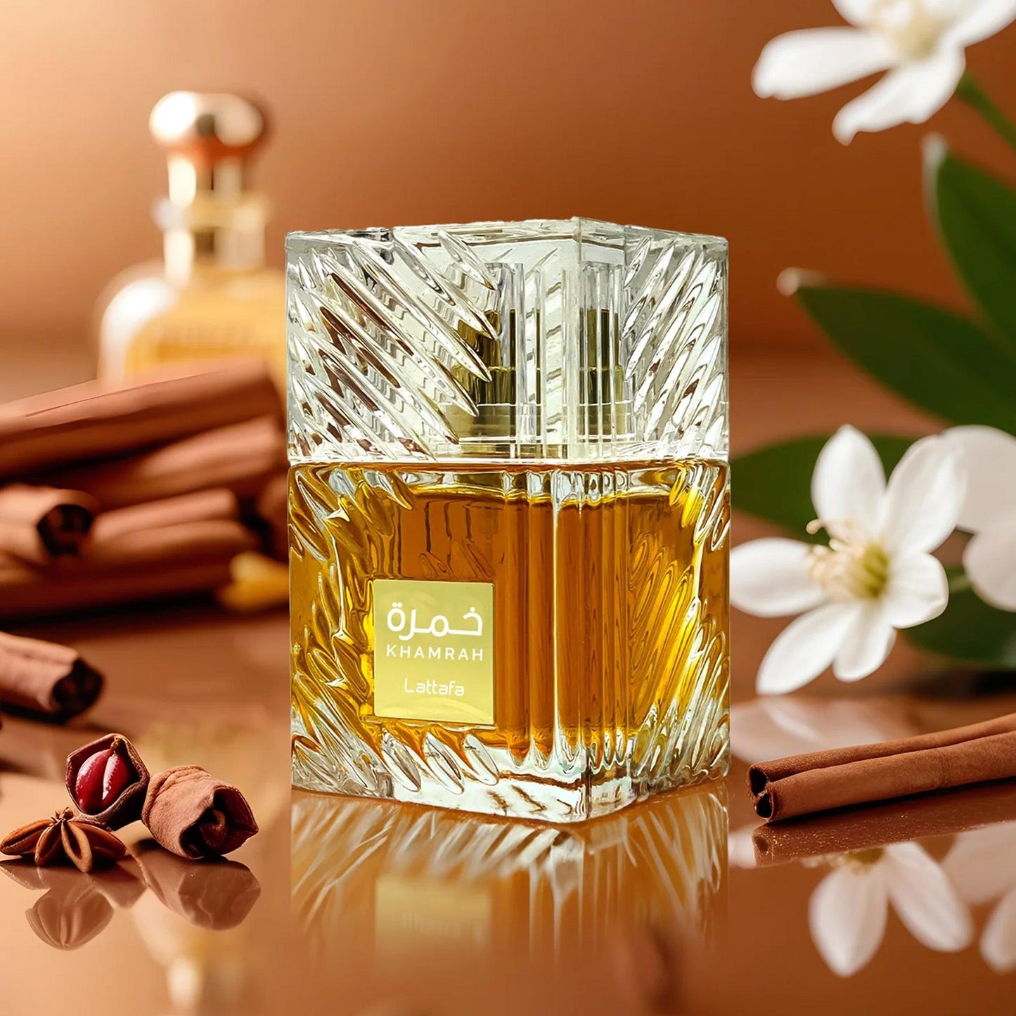 Lattafa Khamrah perfume bottle with amber liquid surrounded by cinnamon and white flowers