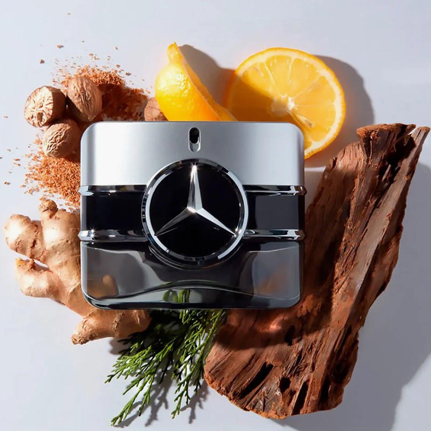 Mercedes-Benz perfume bottle with a sleek silver and black design placed on a white surface surrounded by fresh orange slices, ginger, nutmeg, and wooden textures