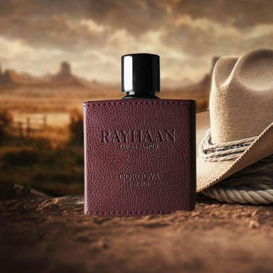 Rayhaan Cordova For Him Eau De Parfum bottle with textured brown leather design placed beside a cowboy hat in a rustic outdoor setting at sunset
