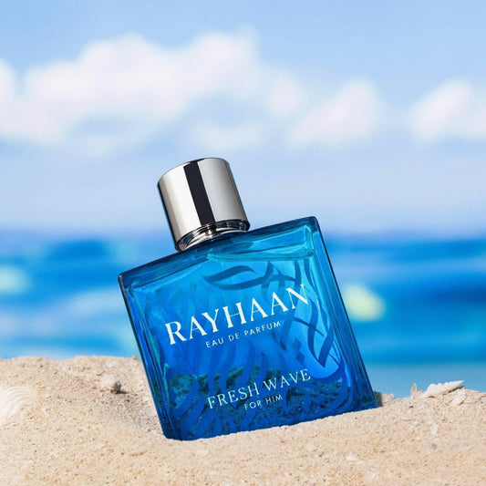 Rayhaan Fresh Wave For Him Eau De Parfum blue glass bottle with silver cap placed on beach sand with the ocean and sky in the background