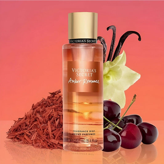 Victoria’s Secret Amber Romance fragrance mist bottle placed beside cherries, vanilla pods, and sandalwood on a glossy surface with a warm orange gradient background