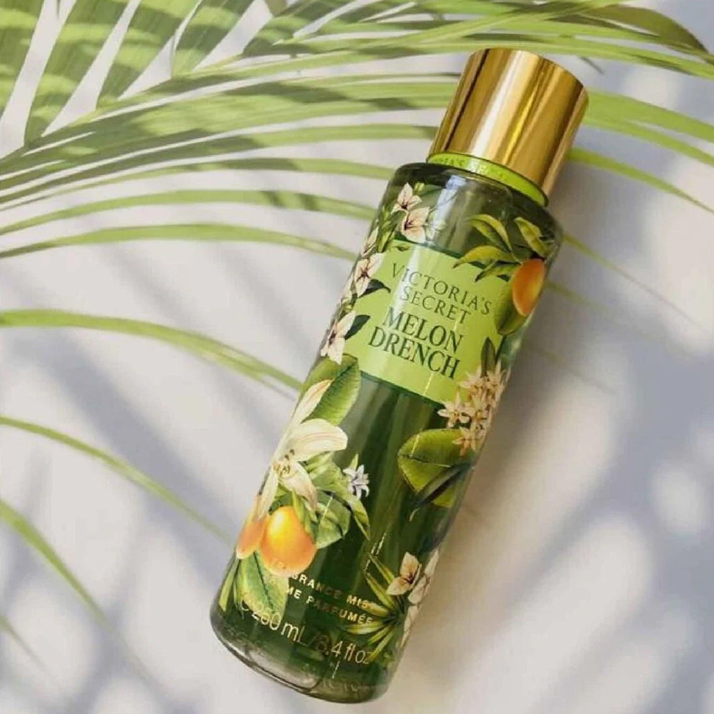 Victorias Secret Melon Drench fragrance mist 250ml bottle with tropical floral design placed under palm leaf shadows on a bright white background
