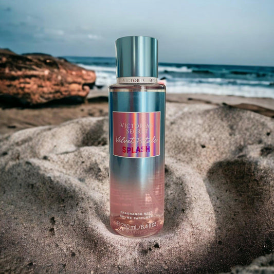 Victoria’s Secret Velvet Petals Splash fragrance mist 250ml bottle placed on sandy beach with ocean waves and rocks in the background