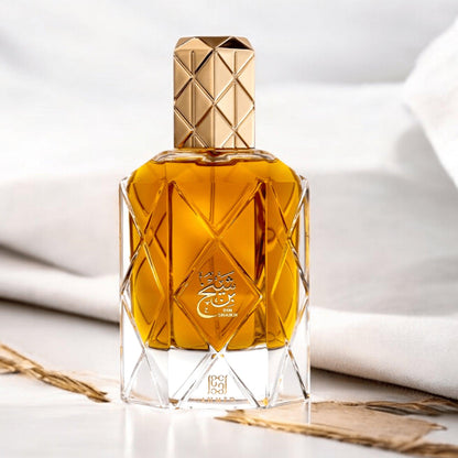 Ahmed Bin Shaikh Eau De Parfum in a golden amber bottle with a geometric glass design and gold cap, placed on a soft white fabric background for a luxurious presentation