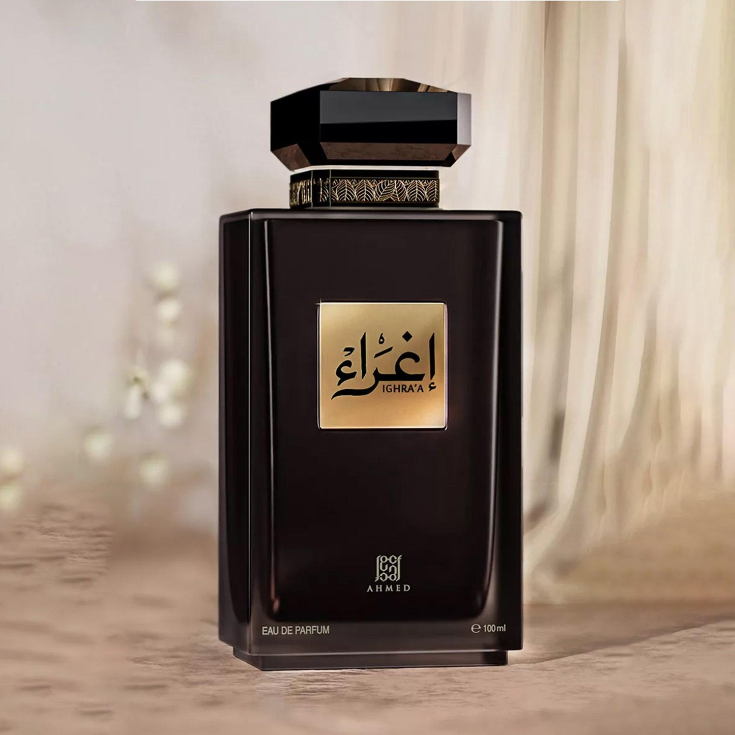 Ahmed Ighraa Eau De Parfum in an elegant black bottle with a gold label and decorative cap, placed against a soft beige curtain backdrop for a luxurious and refined presentation