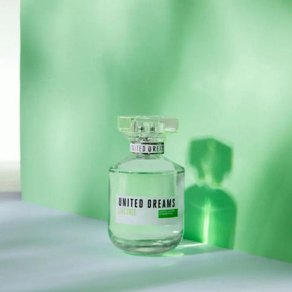 United Colors of Benetton United Dreams Live Free perfume bottle with a light green hue, placed against a matching green backdrop that reflects a soft, refreshing glow