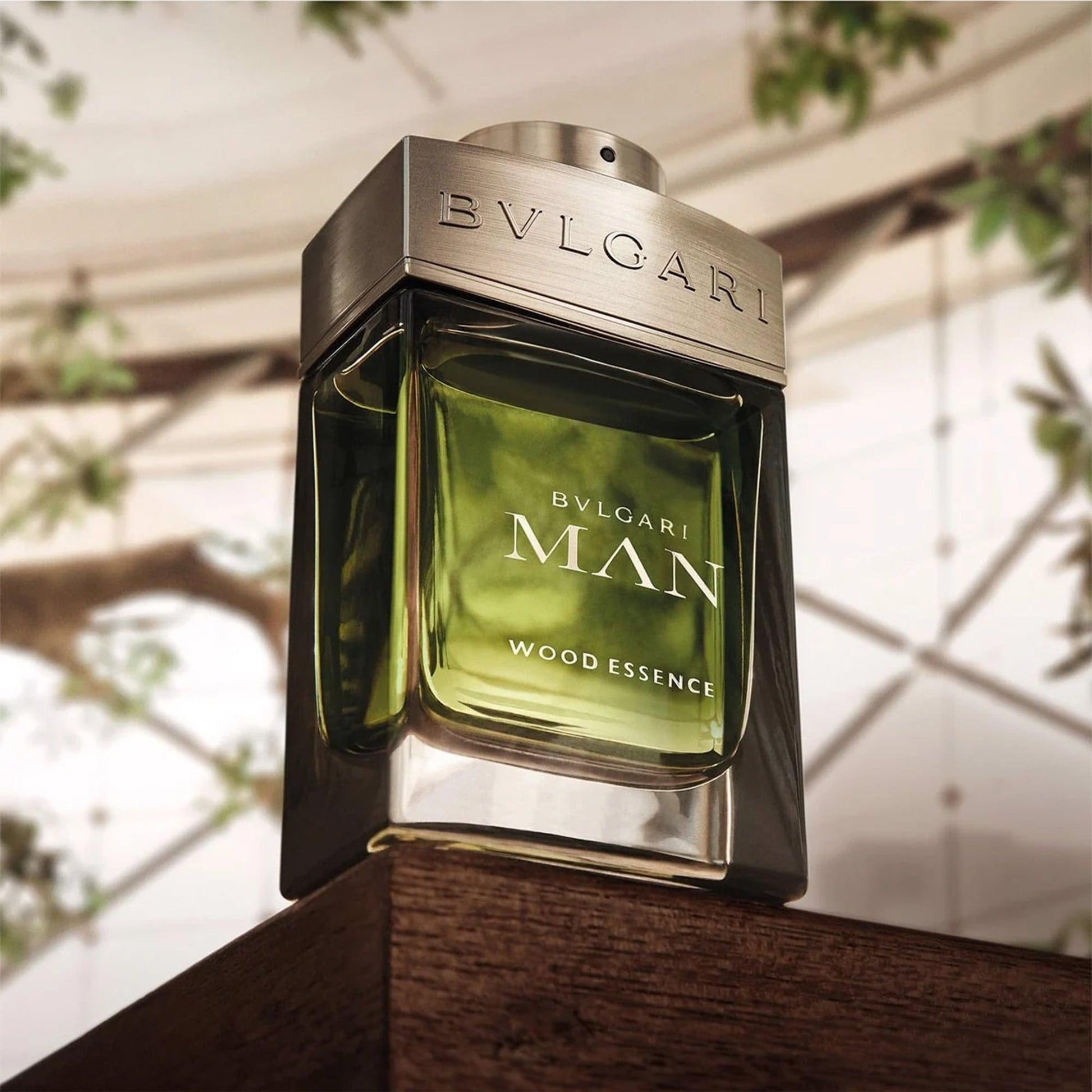 Bvlgari Man Wood Essence Eau De Parfum green glass bottle with metallic cap placed on wooden surface and blurred nature background