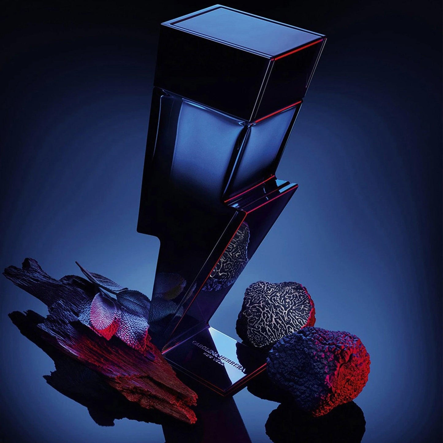 Carolina Herrera Bad Boy Le Parfum lightning bolt-shaped dark blue bottle with truffle and wood accents on illuminated blue background