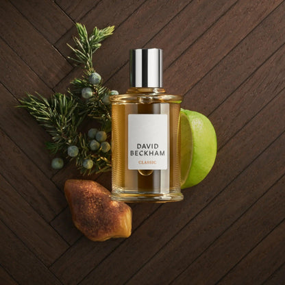 David Beckham Classic perfume bottle with green apple, amber, and juniper berries on a wooden textured surface, symbolizing a fresh, woody masculine fragrance style