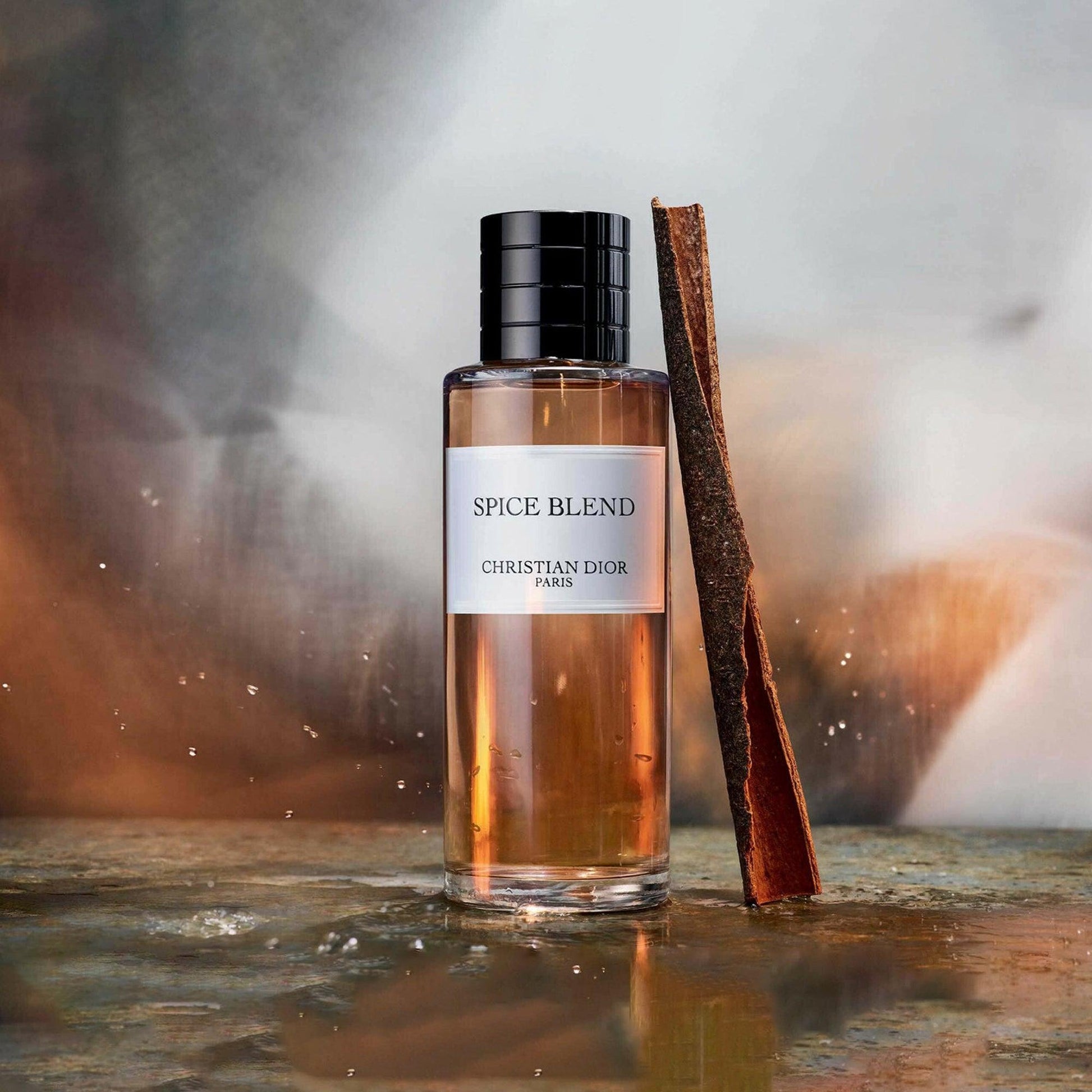 Christian Dior Spice Blend Eau De Parfum bottle with amber liquid placed beside a cinnamon stick on a reflective surface with a warm blurred background
