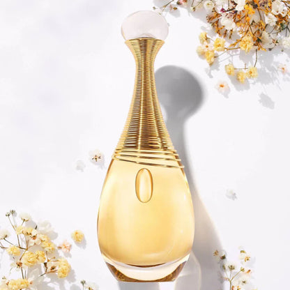 Christian Dior J’adore Eau De Parfum bottle in gold tones placed on a white surface with delicate yellow and white flowers surrounding it