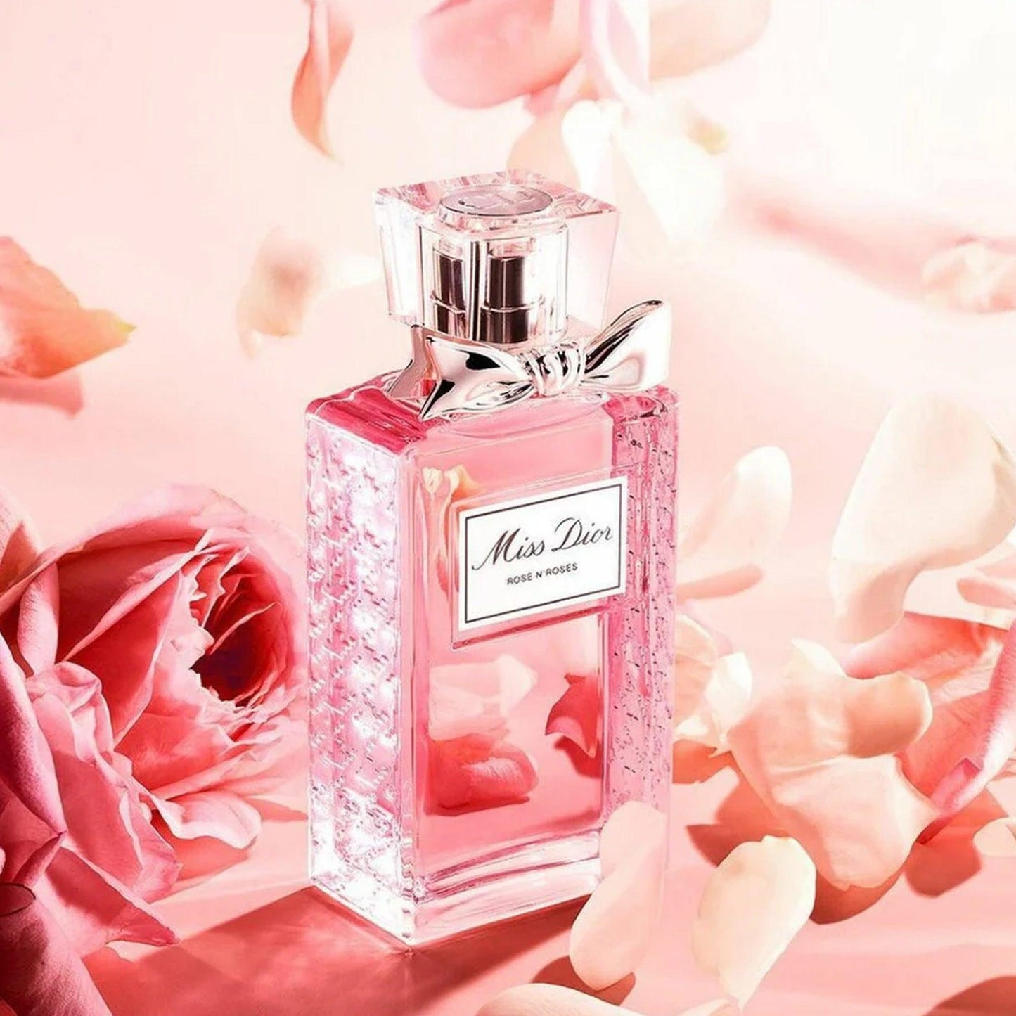 Miss Dior Rose N’Roses Eau De Toilette pink perfume bottle surrounded by soft rose petals on a pastel pink background