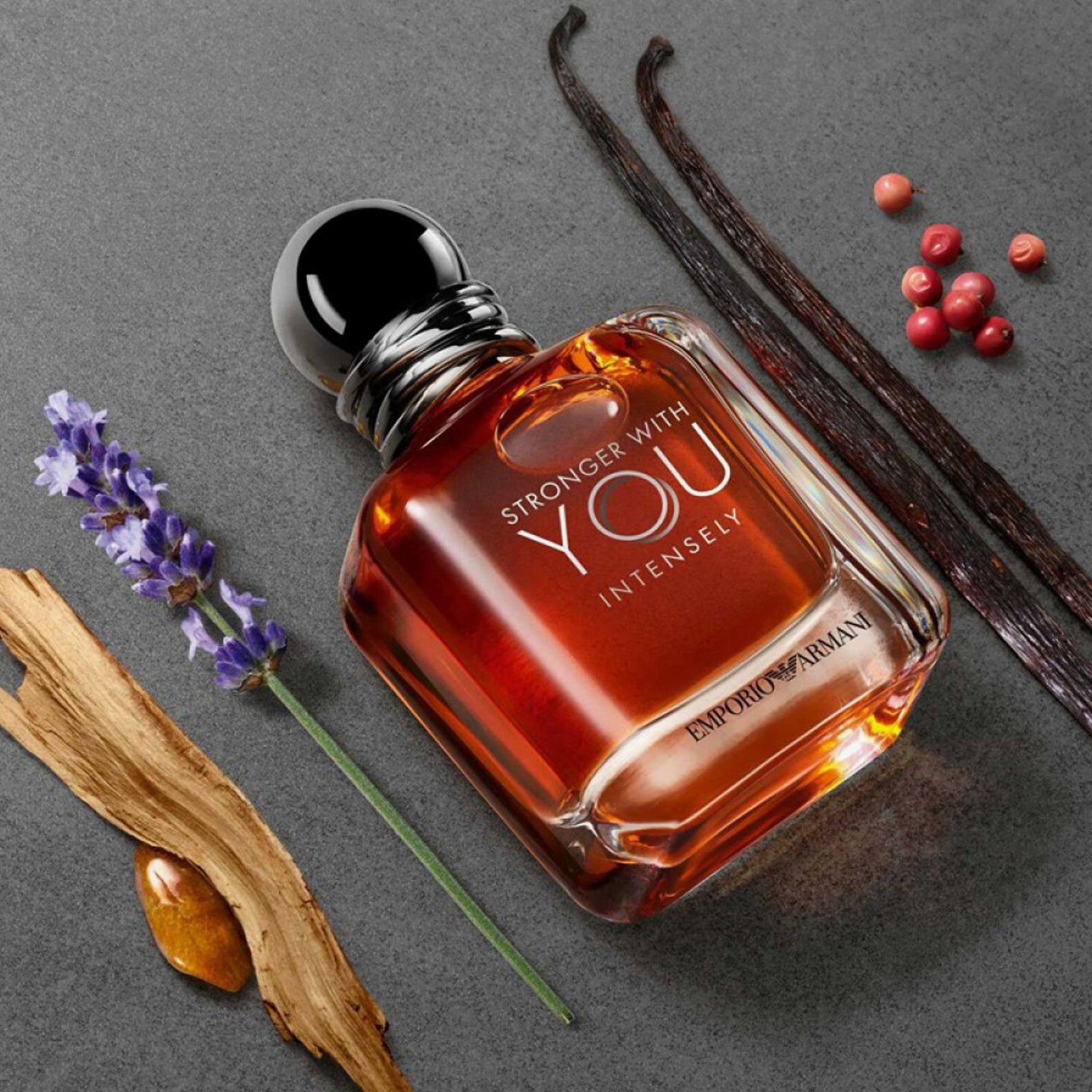 Emporio Armani Stronger With You Intensely Eau De Parfum bottle placed on a grey surface surrounded by vanilla pods, lavender, wood, amber, and peppercorns
