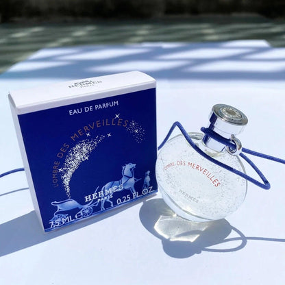 Hermès L’Ombre Des Merveilles Eau De Parfum mini bottle and box placed on a white surface under natural sunlight with blue shadows.