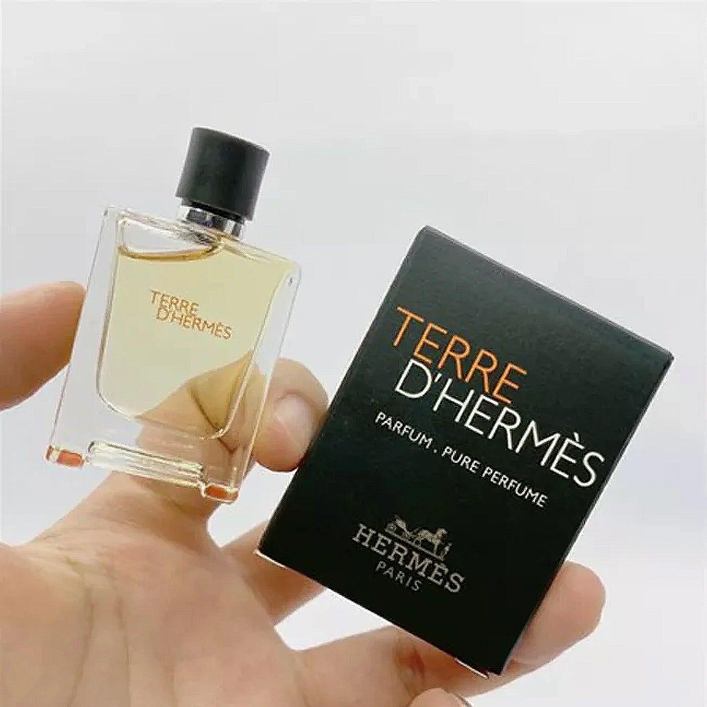 Terre d’Hermès Pure Perfume miniature bottle held in hand beside its black box packaging, showcasing the luxury Hermès Paris branding in a minimalist style