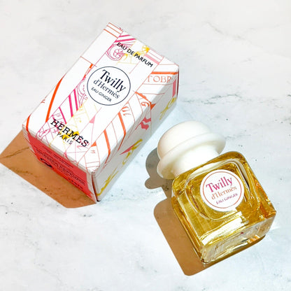 Hermès Twilly d’Hermès Eau Ginger Eau De Parfum bottle and box displayed on a white marble surface with warm lighting.