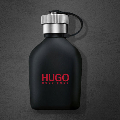 Hugo Boss Just Different Eau De Toilette black matte bottle with silver cap and red logo placed on a dark textured background.