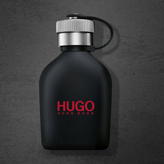 Hugo Boss Just Different Eau De Toilette black matte bottle with silver cap and red logo placed on a dark textured background.