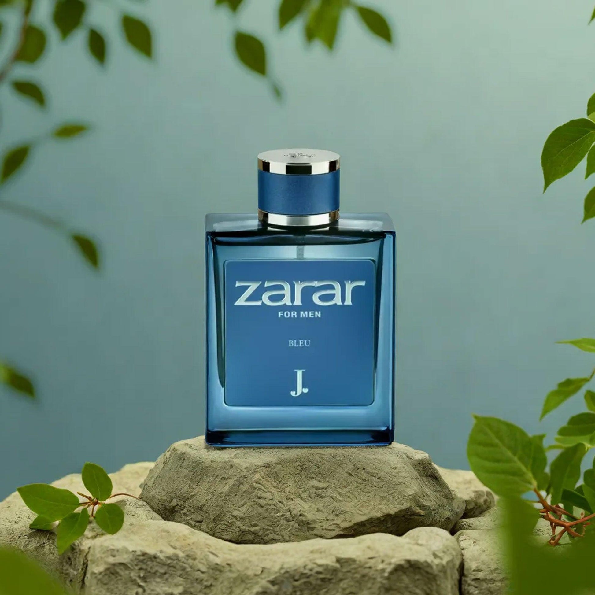 Zarar Bleu For Men Eau De Parfum bottle in blue, displayed on a stone pedestal surrounded by green leaves and soft blue background