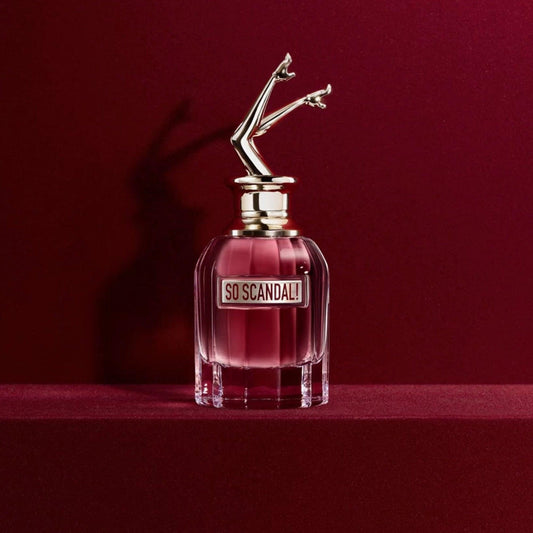 Jean Paul Gaultier So Scandal! Eau De Parfum with a playful leg-shaped cap, placed on a red velvet surface with a deep red background