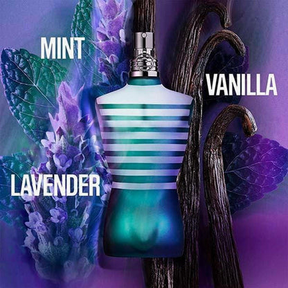 Jean Paul Gaultier Le Male perfume bottle in blue torso design surrounded by mint leaves, lavender flowers, and vanilla pods on a purple background