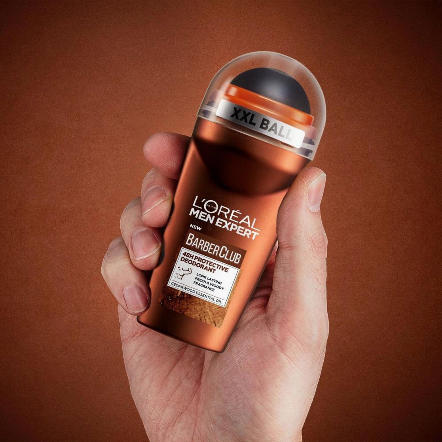 Hand holding L’Oreal Men Expert BarberClub deodorant with copper bottle on brown background