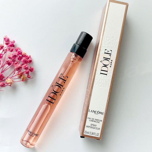 Lancôme Idôle Aura Eau De Parfum 10ml spray bottle with rose gold packaging, placed next to pink flowers on a white background