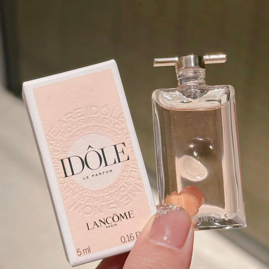 Lancôme Idôle Le Parfum 5ml bottle held by hand beside its pink and white packaging box with soft background
