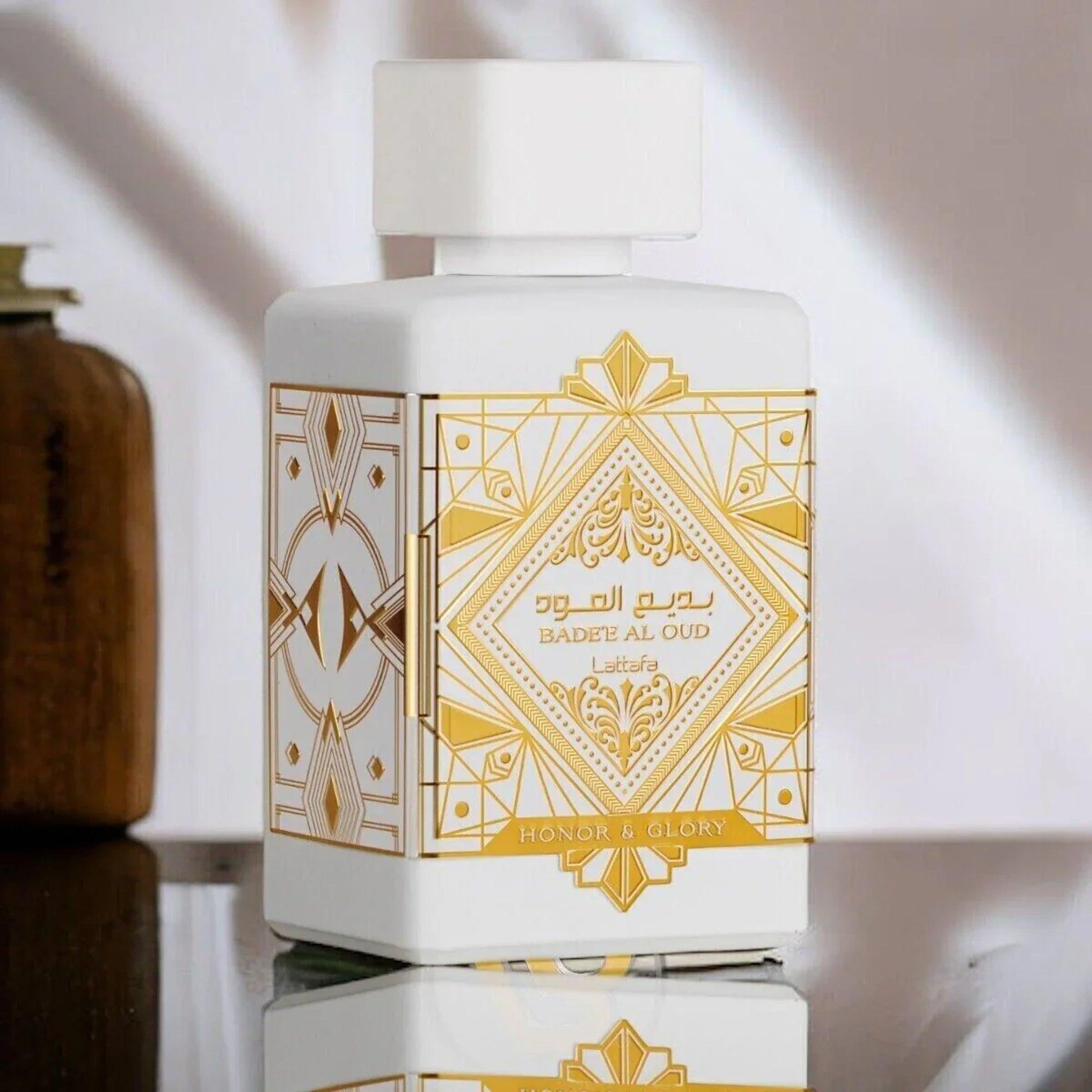Lattafa Badee Al Oud Honor & Glory perfume bottle in elegant white and gold design, placed on a reflective surface with soft lighting to highlight its luxurious details
